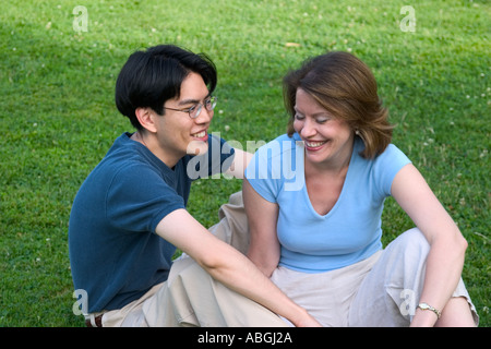 Interracial couple sitting on a lawn in a park Stock Photo
