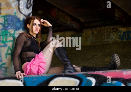 Alternative girl sitting under a bridge covered in graffiti Stock Photo