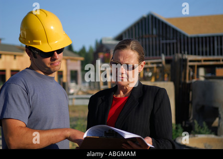 Contractor foreman in hard hat discussing construction plans with the female architect outdoors at the construction site Stock Photo