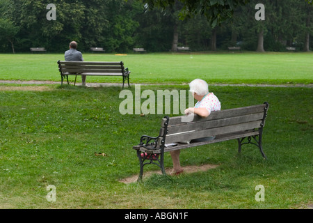 Elderly woman and middle age man sitting on separate wooden benches at a park Stock Photo