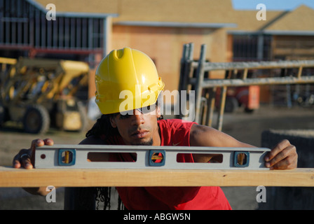 Black construction worker in hard hat checking the level of a plank of wood at job site Stock Photo