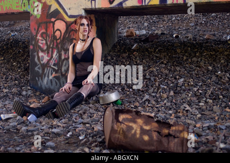 Alternative girl sitting under a bridge covered in graffiti Stock Photo