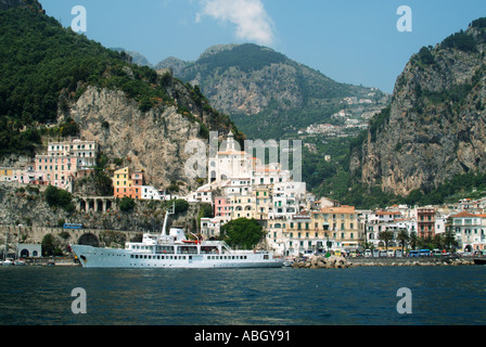 Amalfi town waterfront anchored sightseeing tour boat named Falerno in front of UNESCO coastline & cliff face buildings at Salerno Campania Italy EU Stock Photo