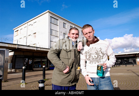 Two unemployed youths aged 19 sat on roadside curb sharing bottle of alcohol in shopping centre on Gurnos Estate Merthyr Tydfil