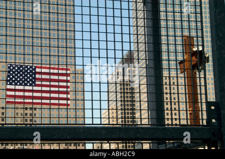 A view through a grid fence of a large rusted cross made of girders from the destroyed twin towers and a large American flag wit Stock Photo