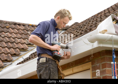 A builder installing brackets to hold a gutter below a roof of a home. Stock Photo