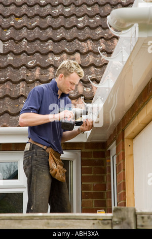 A builder installing brackets to hold a gutter below a roof of a home. Stock Photo