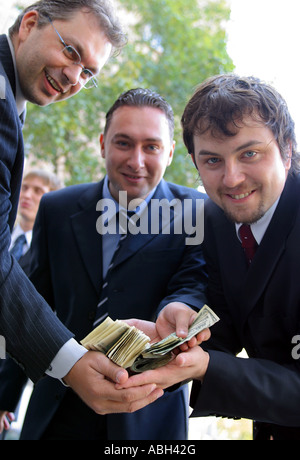 A portrait of three businessmen in suits seen here holding a large amount of dollar bills. Stock Photo