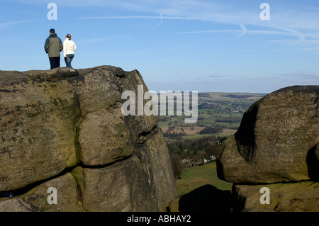 Walkers standing on and looking over the edge of Cow and Calf Rocks, Ilkley, West Yorkshire, UK. Stock Photo