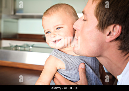 Portrait of father and son in kitchen, man kissing his baby, indoors Stock Photo