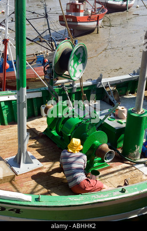 FISHERMAN PAINTING TRAWLER FISHING BOAT'S WINCH WITH GREEN PAINT AT LOW TIDE  ERQUY  HARBOUR BRITTANY FRANCE Stock Photo