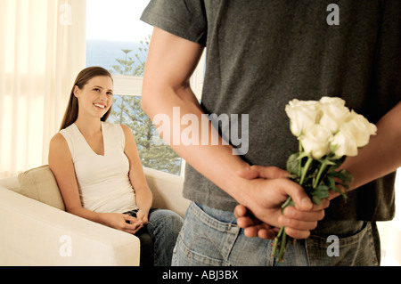 Man hiding bunch of flowers behind his back, facing smiling woman Stock Photo