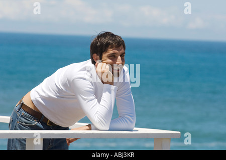 Young smiling man leaning against balustrade, sea in background Stock Photo