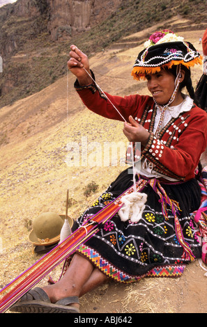 Pisac, Peru. Quechua Indian woman in traditional dress weaving a strap and spinning. Stock Photo
