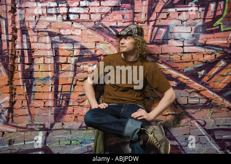 Young man sitting in front of graffitied wall Stock Photo