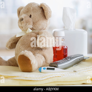 Teddy bear medication thermometer and telephone on blanket Stock Photo