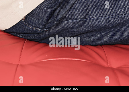 Detail Of Man Wearing Blue Jeans Sitting On Red Leather Sofa Stock Photo