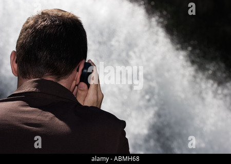 Man In Front Of Waterfall Talking On Mobile Phone Stock Photo