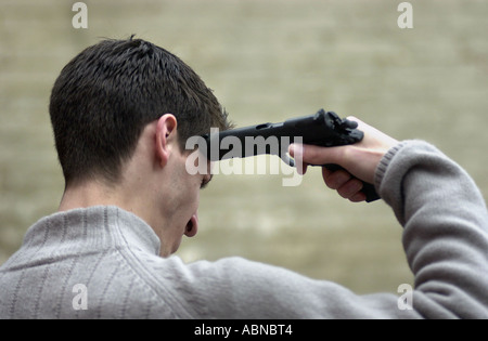 Young man aims a hand gun at his head in a suicide pose UK Stock Photo