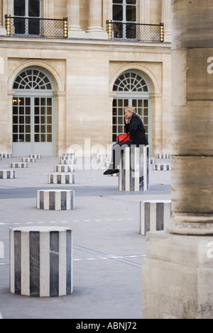 Woman talking on cell phone sits on sculpture column at Palais Royal Paris France Stock Photo