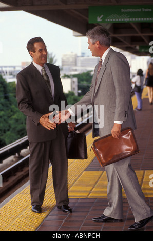 Two executives shake hands on railway platform Stock Photo