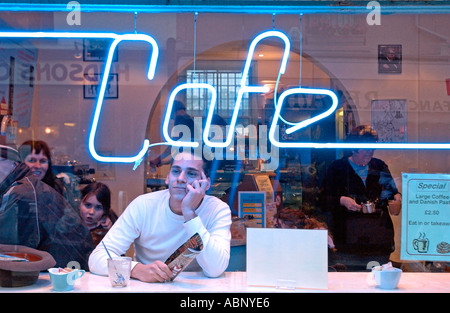 Young city dweller gazing out of coffee bar window with neon sign Stock Photo
