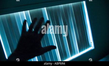 mysterious hand reaching out to venetian blinds Stock Photo
