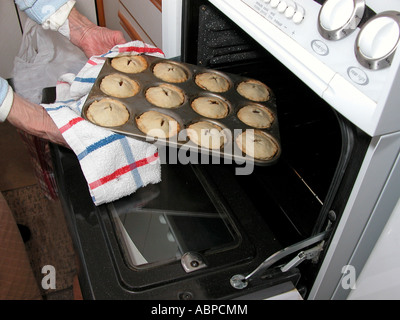 elderly woman taking cooked pastry pies out of the oven in kitchen Stock Photo