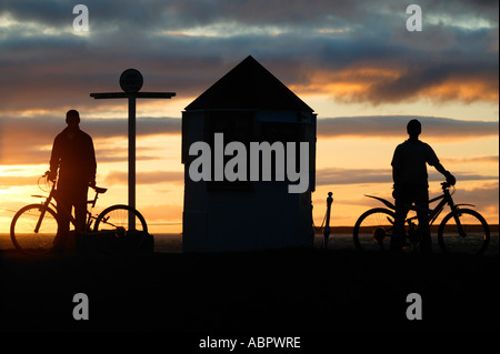 Two boys with bicycles in silhouette at Sunset, John o' Groats Caithness, Highlands, North Scotland UK Europe