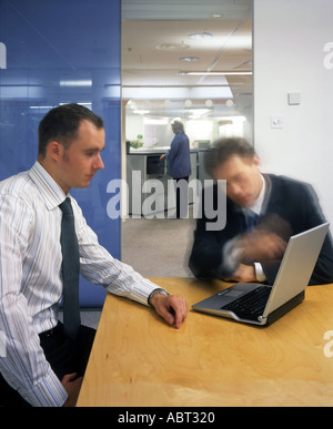 Office life and interiors. Two businessmen sitting at meeting table and woman by filing cabinets in background. Stock Photo