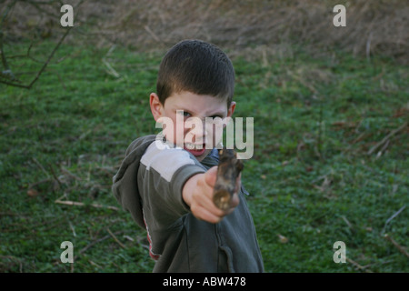 A 6 year old boy uses a stick as a gun whilst playing, UK. Stock Photo