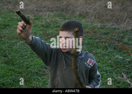 A 6 year old boy uses a stick as a gun whilst playing, UK. Stock Photo