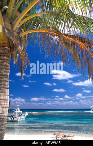 Caribbean Cayman Islands Cayman Brac beach boats palm tree clear water and blue sky man in lounge chair relaxing on beach Stock Photo