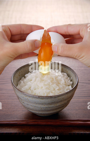 A woman cracking an egg above steamed rice Stock Photo