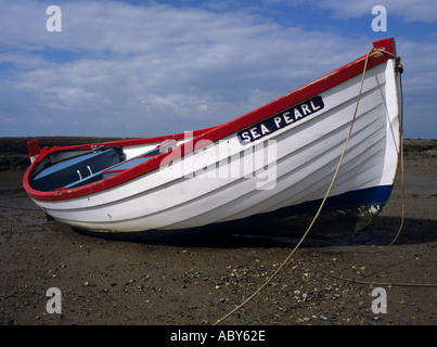 NORFOLK UK March Lone red and white rowing boat left high and dry Stock Photo