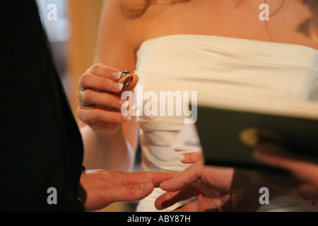 A bride and groom exchange wedding rings bands during their church marriage ceremony UK wife putting ring on husbands finger Stock Photo