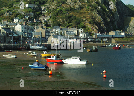 Barmouth moored fishing boats and small yachts in the Afon Mawddach estuary railway viaduct train and footbridge beyond Stock Photo