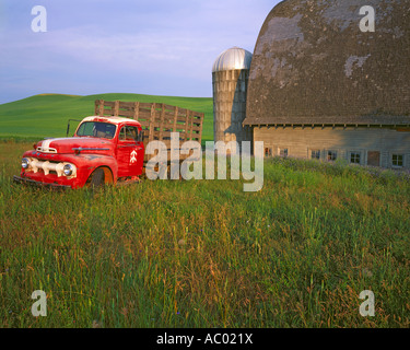 Whitman County WA Vintage red Ford flatbed truck parked in front of a weathered barn and silo in summer Stock Photo