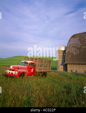 Whitman County WA: Vintage red Ford flatbed truck parked in front of a weathered barn and silo in summer Stock Photo