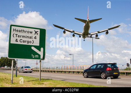 Road sign on the A4 for Heathrow airport with a low flying plane passing over head Stock Photo