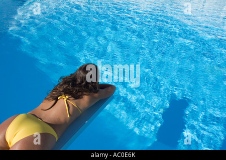 Young woman lying on diving board over pool Stock Photo