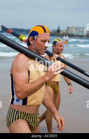 Surf lifesavers in club colours carry oars on their shoulders on Cronulla Beach The lifesavers are competing in surfboat races Stock Photo