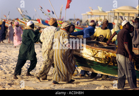 Fishermen bring a boat up onto the sands of the Plage des Pecheurs Fishermen s Beach near Nouakchott Stock Photo