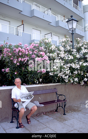 An elderly man with his newspaper on a bench on the waterfront in Grado, Italy. Stock Photo