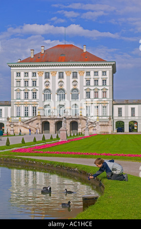 BOY PLAYING WITH DUCKS ON POND IN FRONT OF  SCHLOSS NYMPHENBURG PALACE MUNICH BAVARIA GERMANY EUROPE Stock Photo