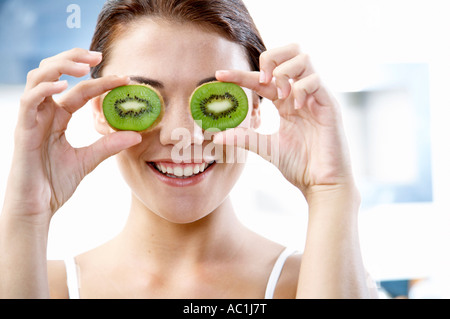 Young woman hiding eyes with kiwis Stock Photo