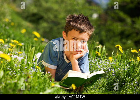 Boy in field reading book, resting head on hand