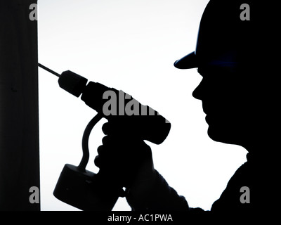 silhouette of builder in safety hard hat drilling a hole in the wall Stock Photo