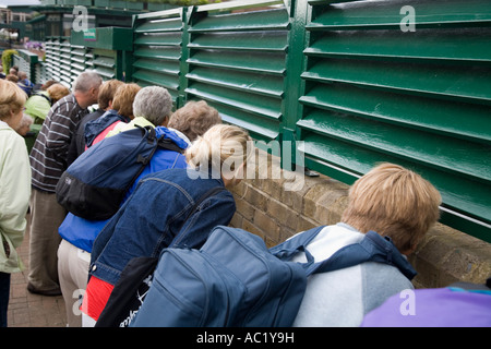 Tennis fans watch play through cracks in the louvre screens during game on outside Court at Wimbledon tennis Championship UK