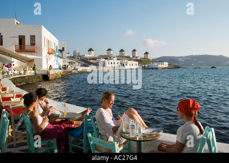 People sitting in restaurants and bars directly at sea windmills in background Little Venice Mykonos Town Mykonos Greece Stock Photo